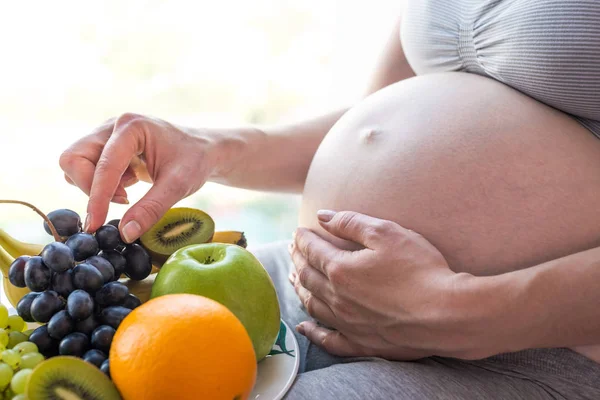 Kobieta w ciąży z brzuchem gospodarstwa talerz z owocami. Koncepcja dla kontroli masy ciała i zdrowe odżywianie w ciąży — Zdjęcie stockowe