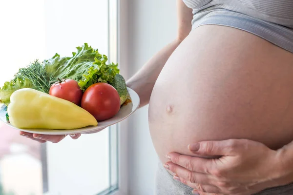 Kobieta w ciąży brzuch gospodarstwa talerz z warzywami. Koncepcja dla kontroli masy ciała i zdrowe odżywianie w ciąży — Zdjęcie stockowe