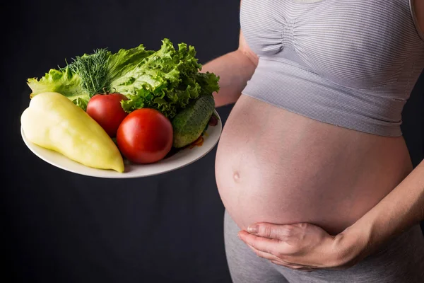 La pancia di donna incinta che tiene un piatto con verdure. Concetto per il controllo del peso e un'alimentazione sana durante la gravidanza — Foto Stock