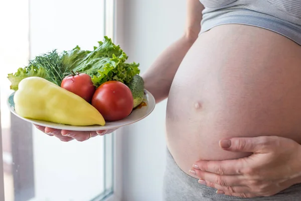 Kobieta w ciąży brzuch gospodarstwa talerz z warzywami. Koncepcja dla kontroli masy ciała i zdrowe odżywianie w ciąży — Zdjęcie stockowe