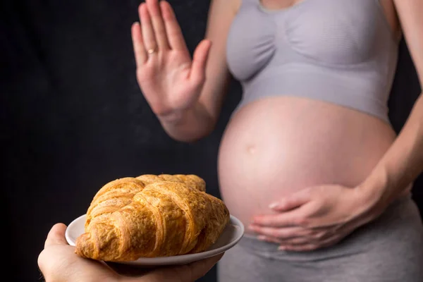 Uma mulher grávida com barriga se recusa a croissants. Conceito de controle de peso e uma dieta não saudável durante a gravidez — Fotografia de Stock