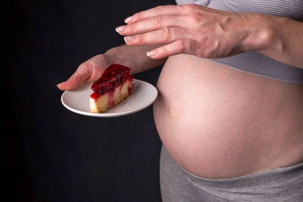 Uma mulher grávida com barriga segurando um pedaço de cheesecake. Conceito de controle de peso e uma dieta não saudável durante a gravidez — Fotografia de Stock