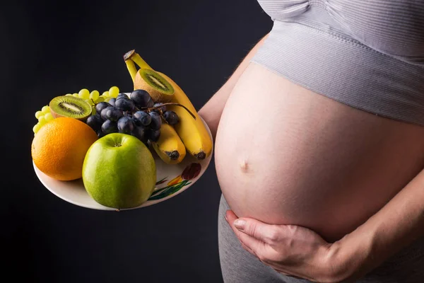 Uma mulher grávida com barriga segurando um prato com frutas. Conceito para controle de peso e alimentação saudável durante a gravidez — Fotografia de Stock