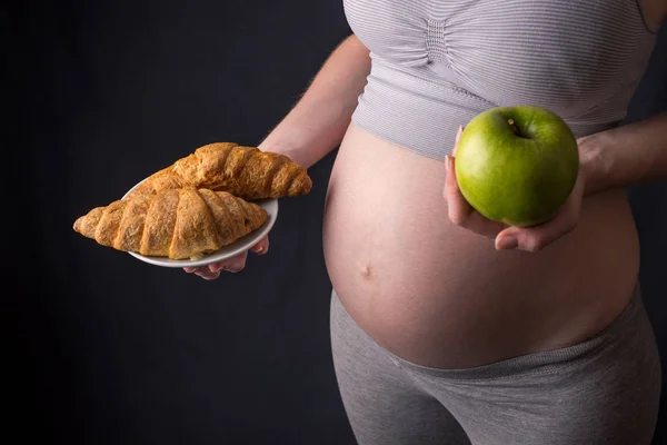 Terhes nő hasa tartja a lemez dzsunka és egészséges élelmiszer. Fogalom megválasztása diéta, a terhesség alatt — Stock Fotó