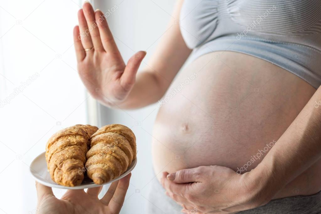 A pregnant woman with belly refuses to croissants. Concept weight control and an unhealthy diet during pregnancy