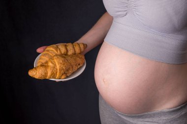 Ay çöreği bir tabak tutarak karın hamile bir kadınla. Kavram kilo kontrolü ve hamilelik döneminde bir sağlıksız diyet