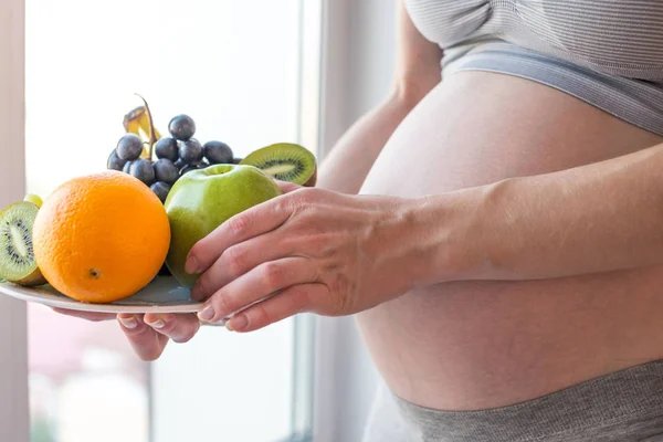 Uma mulher grávida com barriga segurando um prato com frutas. Conceito para controle de peso e alimentação saudável durante a gravidez — Fotografia de Stock