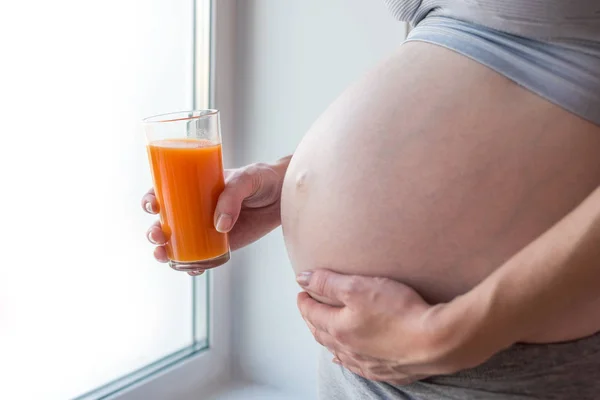 Kobieta w ciąży z brzuchem w ręku trzymając szklankę soku z marchwi. Koncepcja dla kontroli masy ciała i zdrowego odżywiania — Zdjęcie stockowe