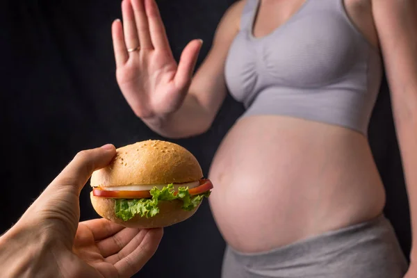 Ciężarna kobieta z brzuchem odmawia burgera. Kontrola koncepcji podczas ciąży — Zdjęcie stockowe