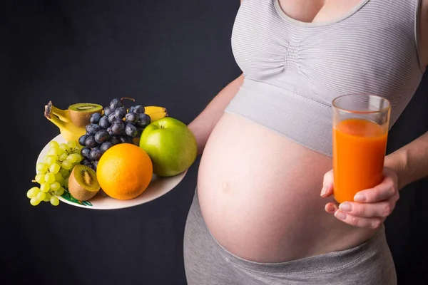 Femme enceinte avec le ventre tenant une assiette avec des fruits et du jus de carotte dans les mains. Concept alimentation saine pendant la grossesse — Photo