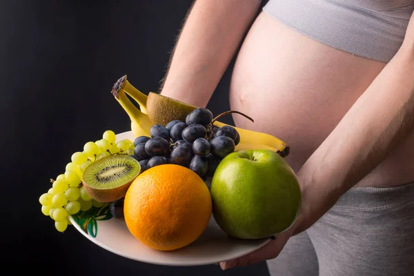 Uma mulher grávida com barriga segurando um prato com frutas. Conceito para controle de peso e alimentação saudável durante a gravidez — Fotografia de Stock