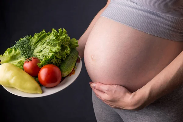 Ventre de femme enceinte tenant une assiette avec des légumes. Concept pour le contrôle du poids et une alimentation saine pendant la grossesse — Photo