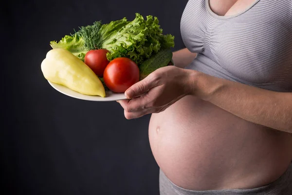 Terhes nő hasa egy tányér zöldséges tartja. Koncepció súlykontroll és az egészséges táplálkozás a terhesség alatt — Stock Fotó