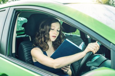 Arabada bir kitap okuma kadını sürücüsü. Dalgın ve tehlikeli sürüş. Trafik ihlali.