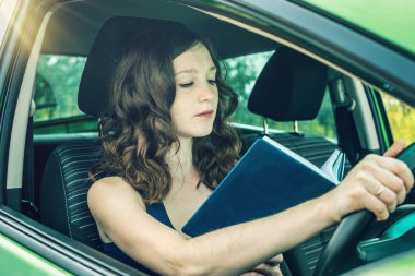 Arabada bir kitap okuma kadını sürücüsü. Dalgın ve tehlikeli sürüş. Trafik ihlali.