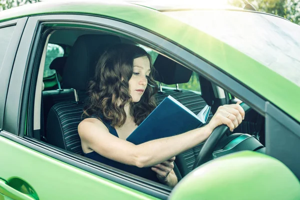 여성 드라이버는 차에서 책을 읽고입니다. 산만 하 고 위험 운전입니다. 교통 위반. — 스톡 사진