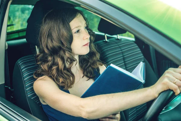 Arabada bir kitap okuma kadını sürücüsü. Dalgın ve tehlikeli sürüş. Trafik ihlali.