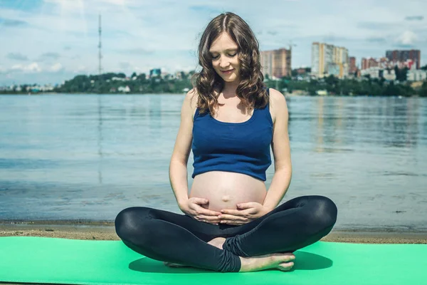 Těhotná žena dělá jógu. Relaxace v přírodě u řeky. — Stock fotografie