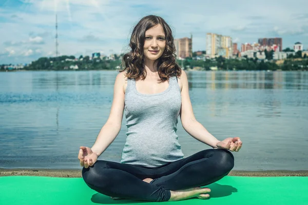 Mujer embarazada haciendo yoga. Relajación en la naturaleza cerca del río . — Foto de Stock