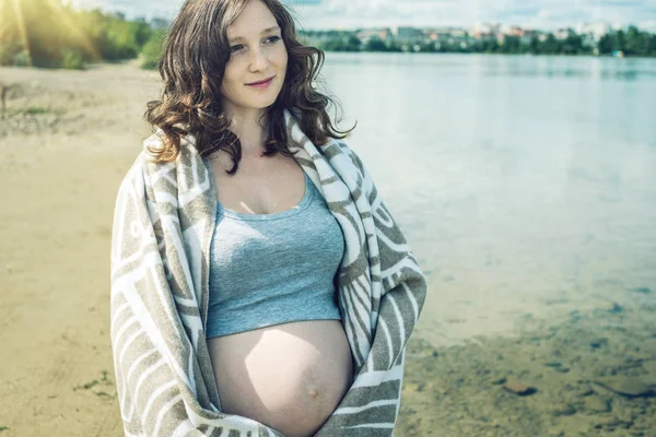 Těhotná procházky po břehu řeky. Zabalený do deky — Stock fotografie