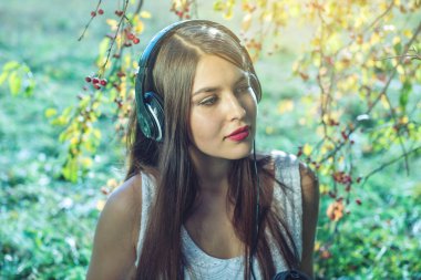 Güneşli bir günde kulaklıklar giyen telefonunuzdaki müziği dinlerken kadın. Sesli kitap ve öğrenci eğitim kavramı