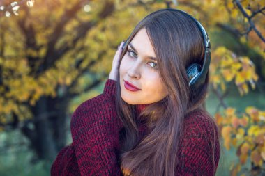 Sonbahar Park ayakta dinleme kadın onun kulaklık ile müzik. İyi bir ruh hali, favori müzik, mutlu zaman kavramı.