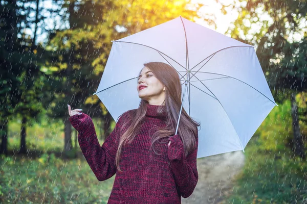 雨の中白い傘と日当たりの良い公園を歩いて幸せな若い女。季節と秋の気分のコンセプト — ストック写真