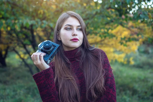 ヴィンテージ レトロなカメラを保持する秋公園で美しい女性。趣味としての写真のコンセプト — ストック写真