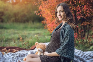 Bir mide ile bekleyen anne battaniye üzerinde oturur ve bebeğe anlatır. Gebelik ve sonbahar uyum kavramı