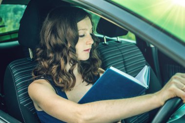 Arabada bir kitap okuma kadını sürücüsü. Dalgın ve tehlikeli sürüş. Trafik ihlali.