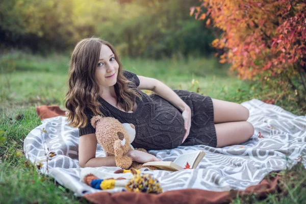 Schwangere mit Bauch liegt auf einer Decke und liest dem Baby Geschichten vor. Konzept von Schwangerschaft und Herbstharmonie — Stockfoto