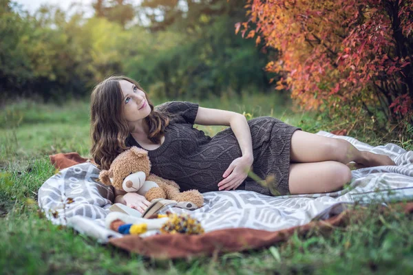 La donna incinta con una pancia giace su una coperta e legge storie al bambino. Concetto di gravidanza e armonia autunnale — Foto Stock