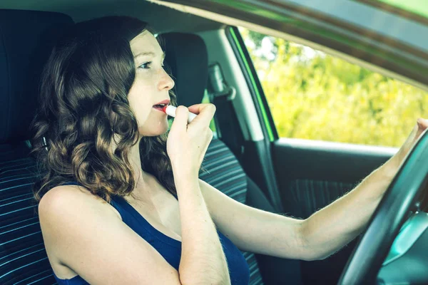 Řidič žena při pohledu do zrcadla a rtěnka v autě. Roztržitý a nebezpečné jízdy. Dopravní přestupky — Stock fotografie