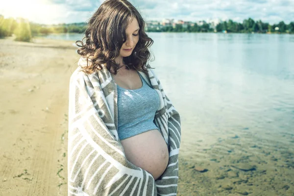 Těhotná procházky po břehu řeky. Zabalený do deky — Stock fotografie