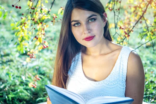 日当たりの良い夏の日に緑の芝生の公園で座っている面白い本を読んで女性。学生教育の概念 — ストック写真