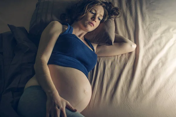 Wanita hamil merasakan sakit di perutnya terbaring di tempat tidur dengan insomnia di malam hari. Konsep kehamilan dan kesehatan Stok Gambar