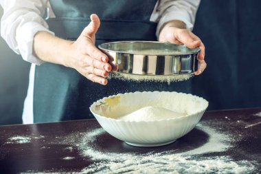 Siyah önlük Şef un hamur pizza için hazırlamak için bir elek ile sifts