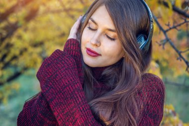 Sonbahar Park ayakta dinleme kadın onun kulaklık ile müzik. İyi bir ruh hali, favori müzik, mutlu zaman kavramı.