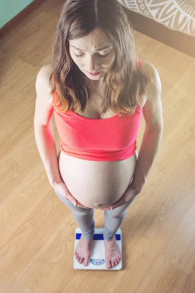 Pregnant woman standing on scales in room. Concept of weight loss and control during pregnancy