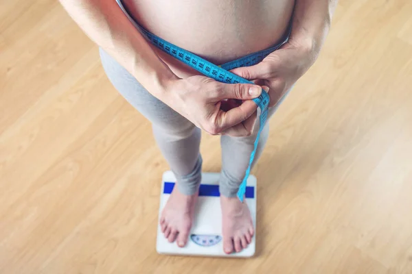 Pregnant woman standing on scales in room. Concept of weight loss and control during pregnancy