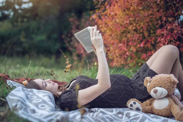 Zwangere vrouw met een buik ligt op een deken en lezen van verhalen aan de baby. Concept van zwangerschap en herfst harmonie — Stockfoto