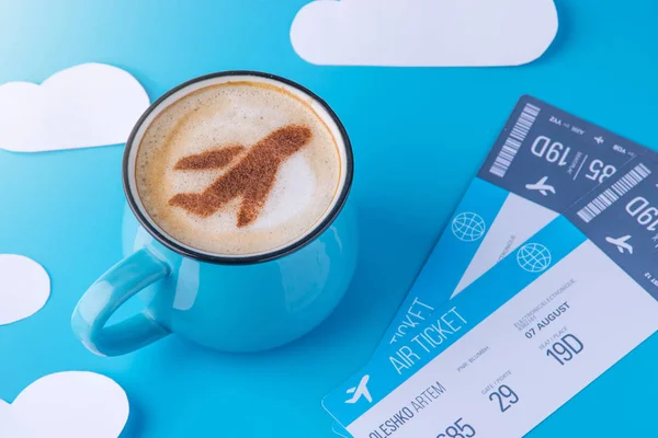 Šálek cappuccino s obrázkem letadla na pěnu a lístky. Pozadí modrá obloha s mraky papíru — Stock fotografie