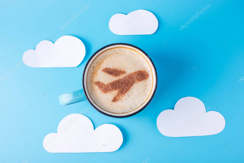 Cup of cappuccino with a picture of the plane on the foam. Blue sky background with paper clouds. Concept of travel