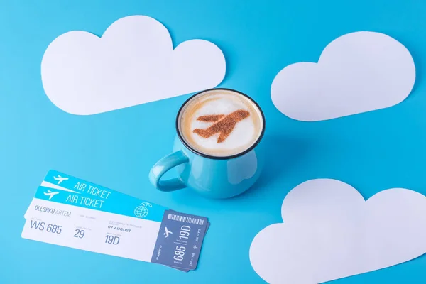stock image Cup of cappuccino with a picture of the plane on the foam and tickets. Blue sky background with paper clouds