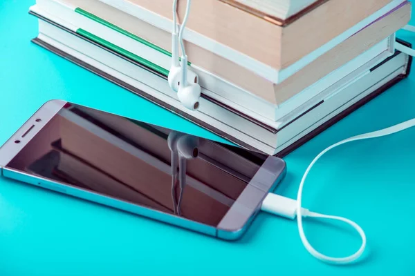 Telefon s bílým sluchátka dále na hromadu knih na modrém pozadí. Koncept audioknih a moderní vzdělávání — Stock fotografie