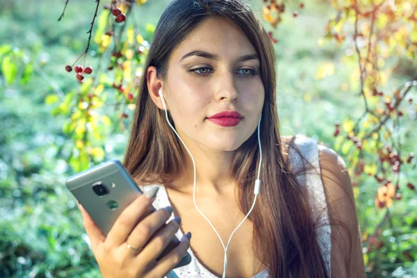 Kobieta, słuchanie muzyki w telefonie, noszenie słuchawek w słoneczny dzień. Koncepcja kształcenia Audiobooki, student — Zdjęcie stockowe