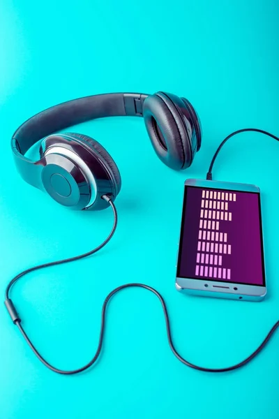 Ecualizador en la pantalla del teléfono con auriculares que reproducen música sobre un fondo azul — Foto de Stock