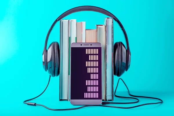 Teléfono con auriculares negros con una pila de libros sobre un fondo azul. Concepto de audiolibros y educación moderna — Foto de Stock