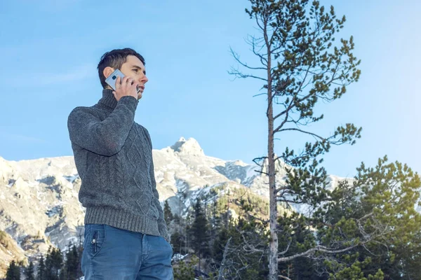 Joven en un suéter con teléfono en la mano en la montaña nevada. Concepto disponibilidad de conexión móvil — Foto de Stock