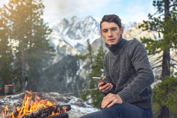 Man sits on the nature of the campfire talking on the phone. Concept of mobile communication, Hiking and outdoor camping